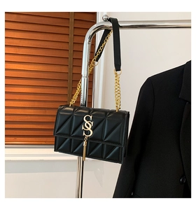 Detail of black quilted shoulder bag with gold metal SS logo and tassel accent