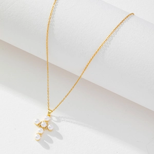 Detail of a gold cross pendant necklace featuring white pearls and tiny zircons