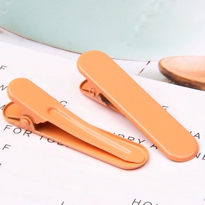 Macro detail of two orange gradient duckbill hair clips on a minimalist background