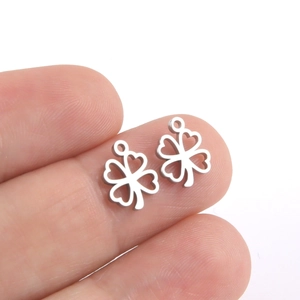 Polished stainless steel four-leaf clover pendant with heart cutouts on a fingertip