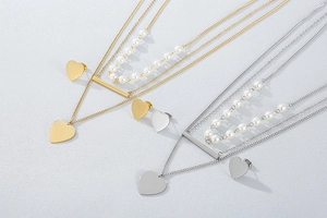 Detail of layered stainless steel heart necklace and stud earrings in gold and silver