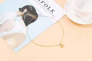 Detailed close-up of golden heart pendant necklace with minimalist design on beige background