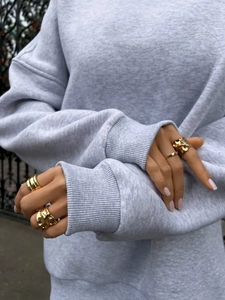 Detail of stacked gold minimalist rings and irregular lava rings on a grey sleeve