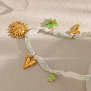 Détail de breloques soleil et cœur en or 18K sur un collier en ruban à motif de feuilles
