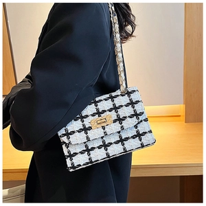 Detail of black and white tweed crossbody bag featuring gold lock and metal chain strap