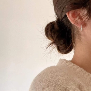 Close-up of minimalist sterling silver wave hoop earrings worn on ear with knitwear