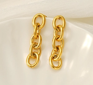 Detail of gold chain drop earrings with textured oval links on a white ceramic plate