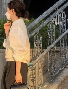 Elegant woman wearing white shirt and beige knit vest paired with black leather handbag