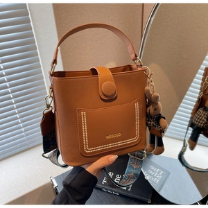 Close-up of caramel leather bucket bag featuring gold logo and printed wide strap