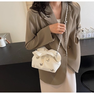 Detail of white pleated bucket bag featuring silver butterfly clasp and chain strap