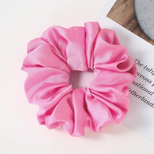 Close-up of pink oversized satin scrunchie with silky pleated texture and decorative card