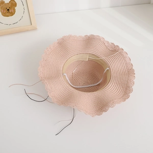 Dettaglio del cappello di paglia rosa con bordo in pizzo ondulato e laccetto antivento