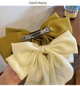 Detail view of large satin bow hair clips in mustard green and cream white with metal spring