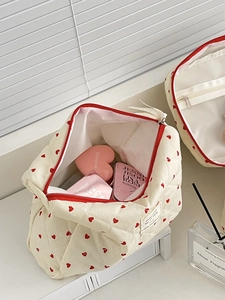 Top view of opened beige quilted makeup bag with red hearts and cosmetic items inside