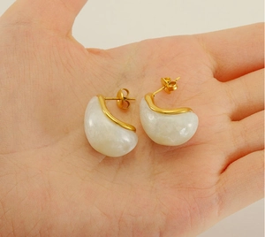 Détail des boucles d'oreilles en résine blanche plaquées or 18 carats sur la main