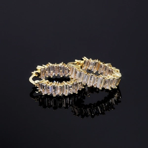 Macro view of gold hoop earrings with baguette-cut white zircon on black reflective background