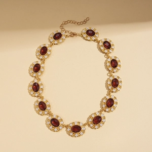 Close-up of vintage oval red gemstone necklace with gold floral border and lobster clasp