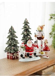 Festive Christmas scene with Santa Claus, angel, and snowman figures on a wooden surface