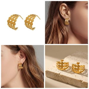 Détails de boucles d'oreilles dorées en C avec motifs ronds ajourés portées par modèle