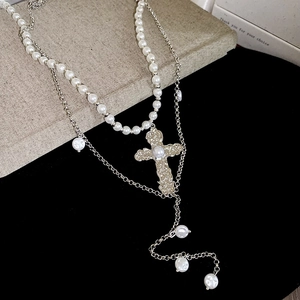 Détail du collier double couche avec pendentif croix vintage et perles blanches élégantes