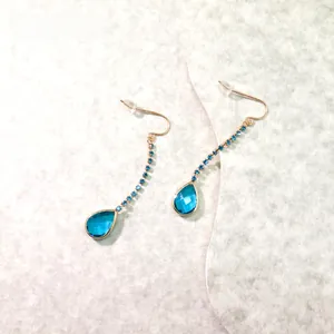 Detail of elegant gold drop earrings with teardrop blue crystal and delicate chain
