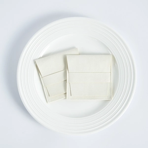 Detail of cream microfiber jewelry pouches with flap closure on a white ceramic plate