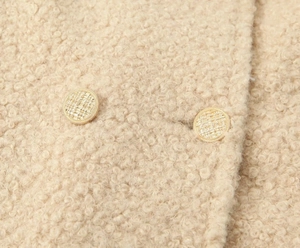 Detail view of apricot boucle coat fabric with a decorative golden embossed metal button