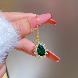 Macro shot of a pear-shaped green emerald pendant surrounded by tiny white diamonds on a gold chain