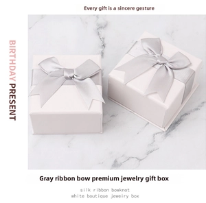 Detail of square white jewelry gift boxes with gray silk bow on marble background
