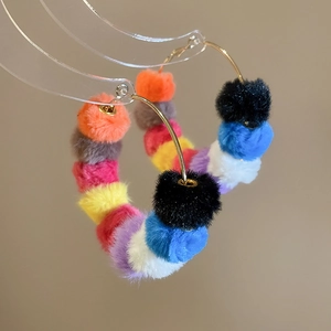 Detail of large hoop earrings with colorful plush fur balls on an acrylic stand