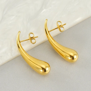 Detail view of gold teardrop earrings with a mirror polished finish on white ceramic