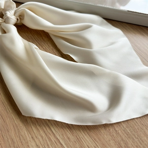 Detailed view of elegant ivory satin hair scrunchie with long ribbon on wooden background