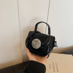 Detail showing the mini black crossbody bag with a hammered silver buckle and smooth finish
