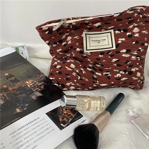 Detail of floral brown pleated makeup bag with PLEASANT TIME label on plush background