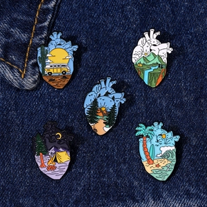 Set of five landscape enamel pins with mountain and forest scenes on denim fabric