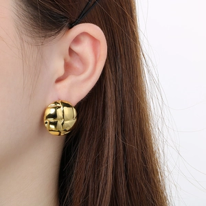 Close-up of golden round stud earrings featuring a textured woven pattern on female model