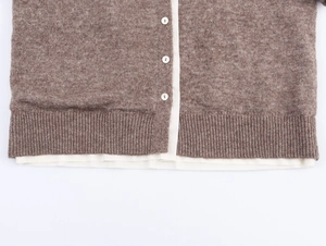 Detail of knit cardigan with white buttons and contrast lining on brown textured fabric