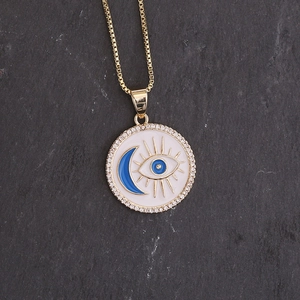 Close-up of 18K gold moon and eye pendant necklace with blue zircon on grey stone