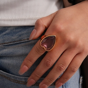Détail d'une bague avec grosse pierre violette en forme de cœur et anneau doré au doigt