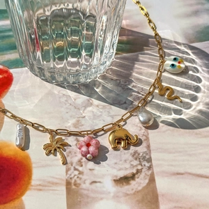 Golden chain necklace featuring baroque pearls, palm tree, and snake charms on marble surface