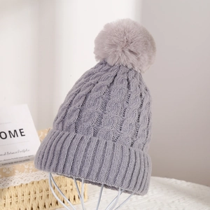 Detail of dark grey knit beanie with fluffy pompom on a white stand for winter