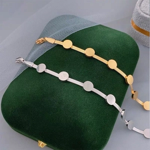Gold and silver snake chain bracelets with round disc charms on green velvet box