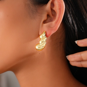 Close-up of gold layered geometric earrings worn by a model in warm side lighting
