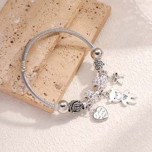 Silver bead bracelet with bear heart and bow charms on a textured stone display