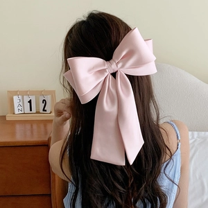 Large pink satin bow hair clip for women shown on back of head in soft home setting