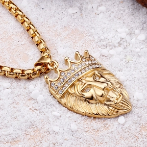 Macro shot of gold lion head pendant with crystal crown on box chain over white stones