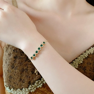 Detailed view of adjustable gold bracelet with seven green cubic zirconia stones and pave halo