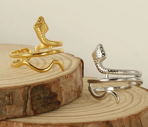 Close-up of gold and silver snake rings on a rustic wooden slice with minimalist background