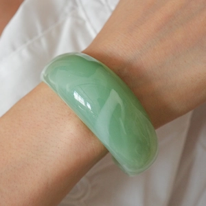 Detailed view of a wide light green resin bangle with a polished, semi-translucent finish