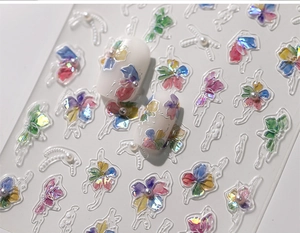 Macro shot of 3D clover nail stickers with iridescent floral patterns and tiny pearls